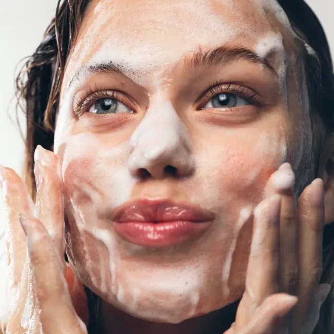 Chica con espuma de limpiador facial en la cara
